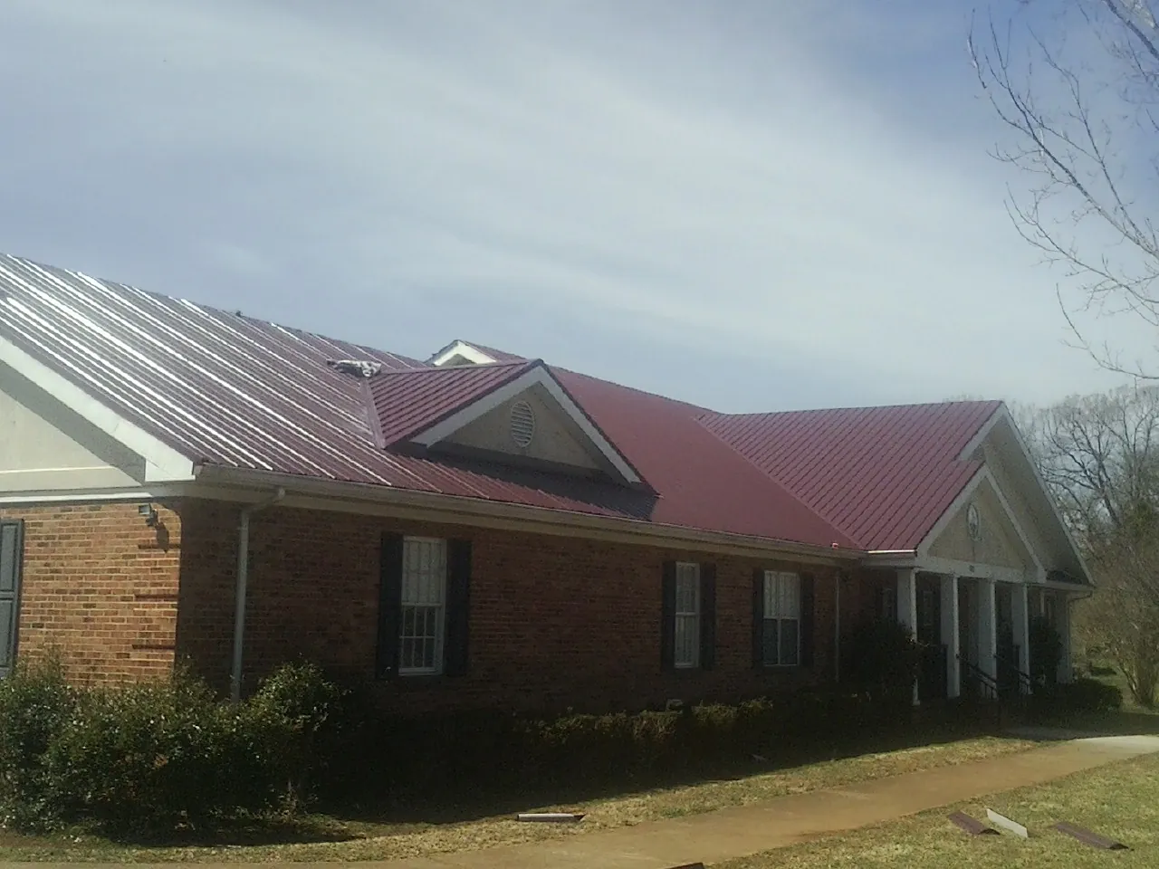 Red metal roof with gabled entries on a long brick building, from a Hail Damage Roof Repair job in Rowena