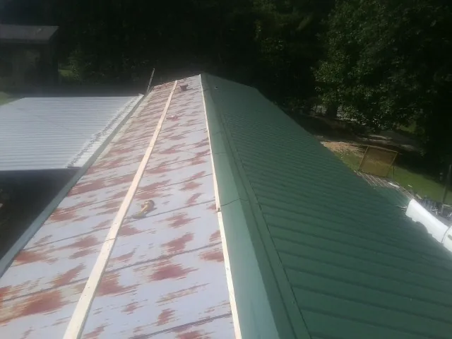 Old rusted panels beside newly installed green metal roofing — Wind Damage Roof Repair by Roofing Brothers in Rowena