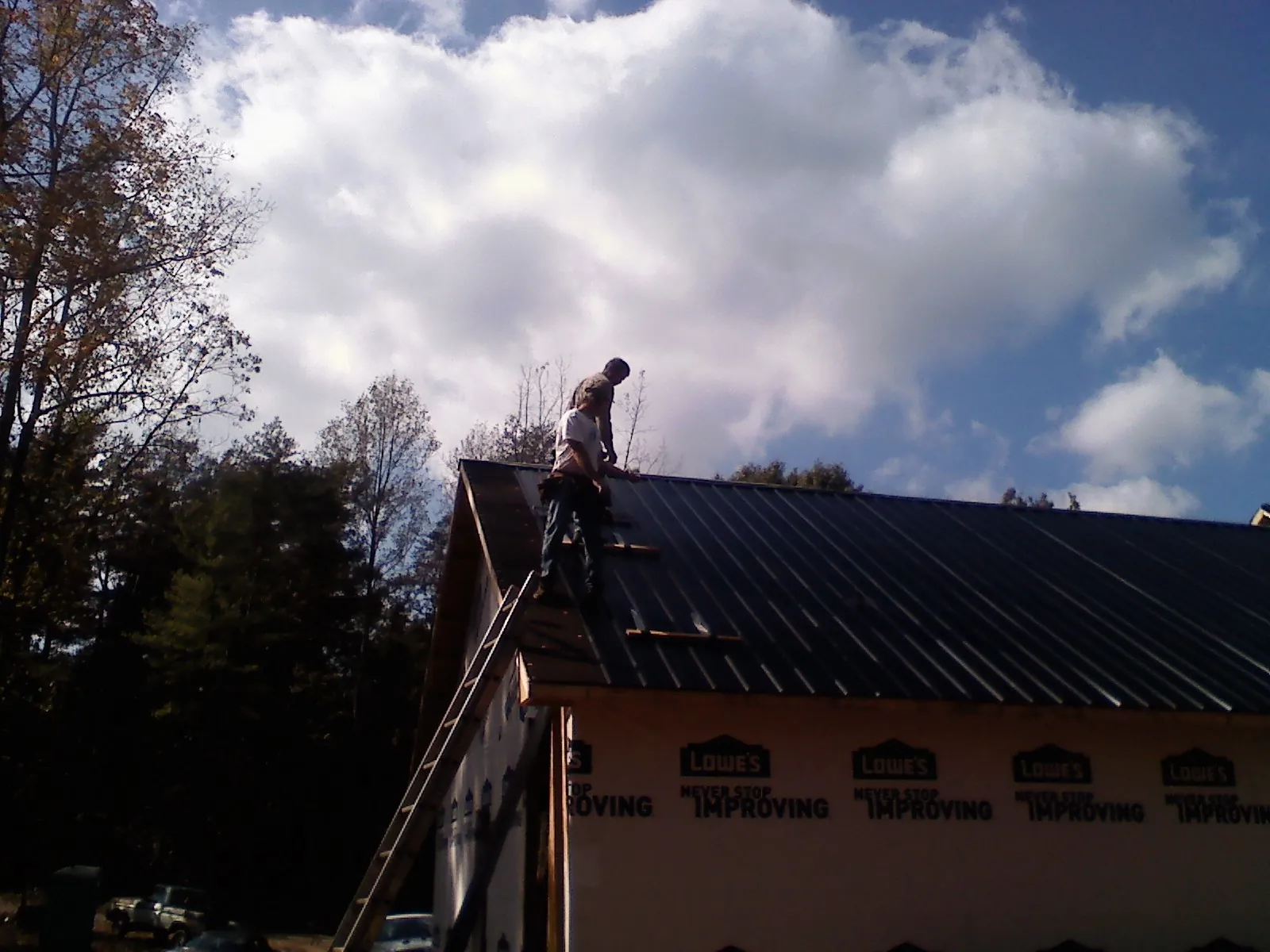 Roofer fastening dark metal panels high against a cloudy sky, from a Roof Inspection job in Rowena