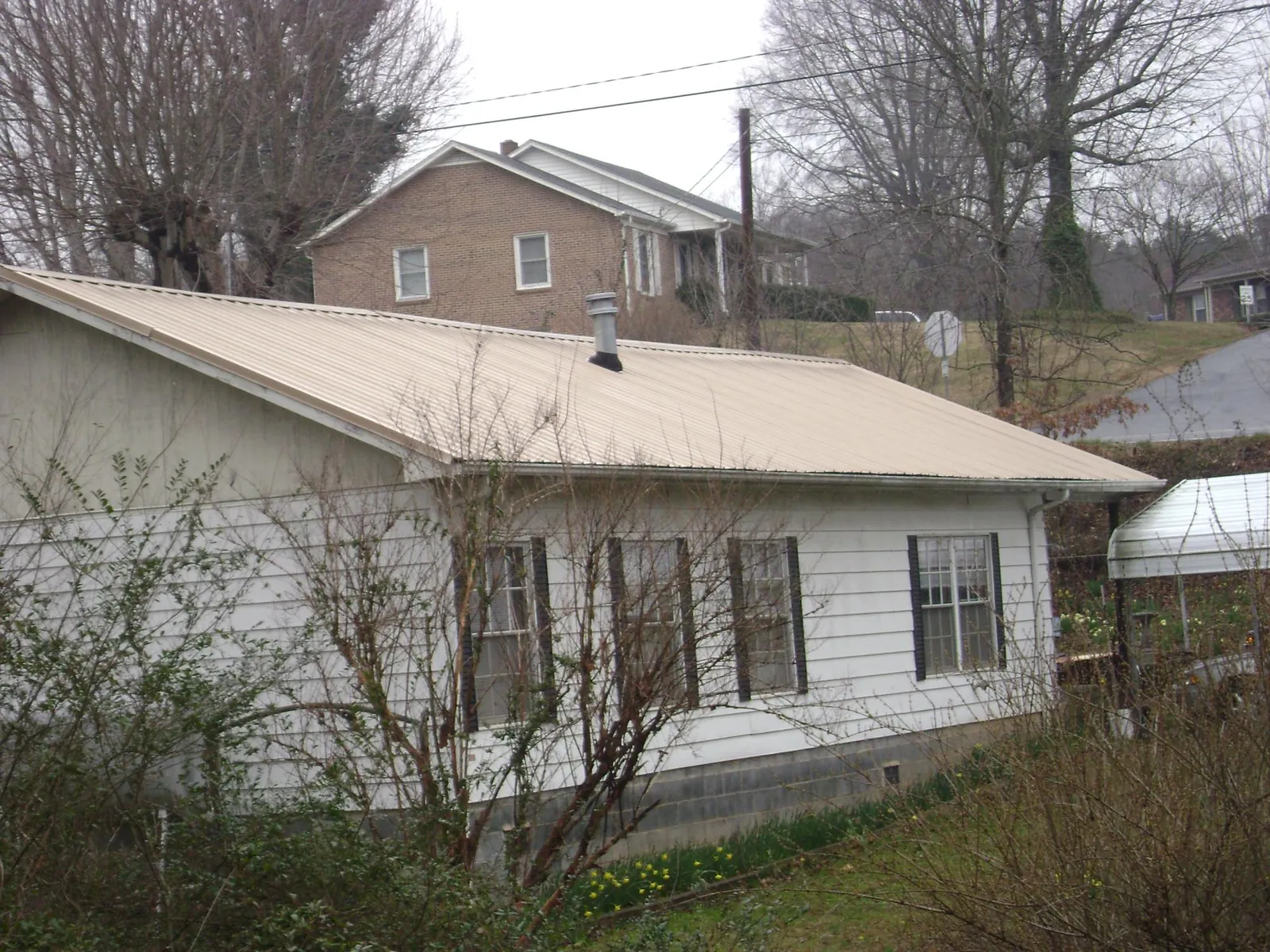 Tan metal roof on a white sided house set into a hillside — Commercial Roofing by Roofing Brothers in Rowena
