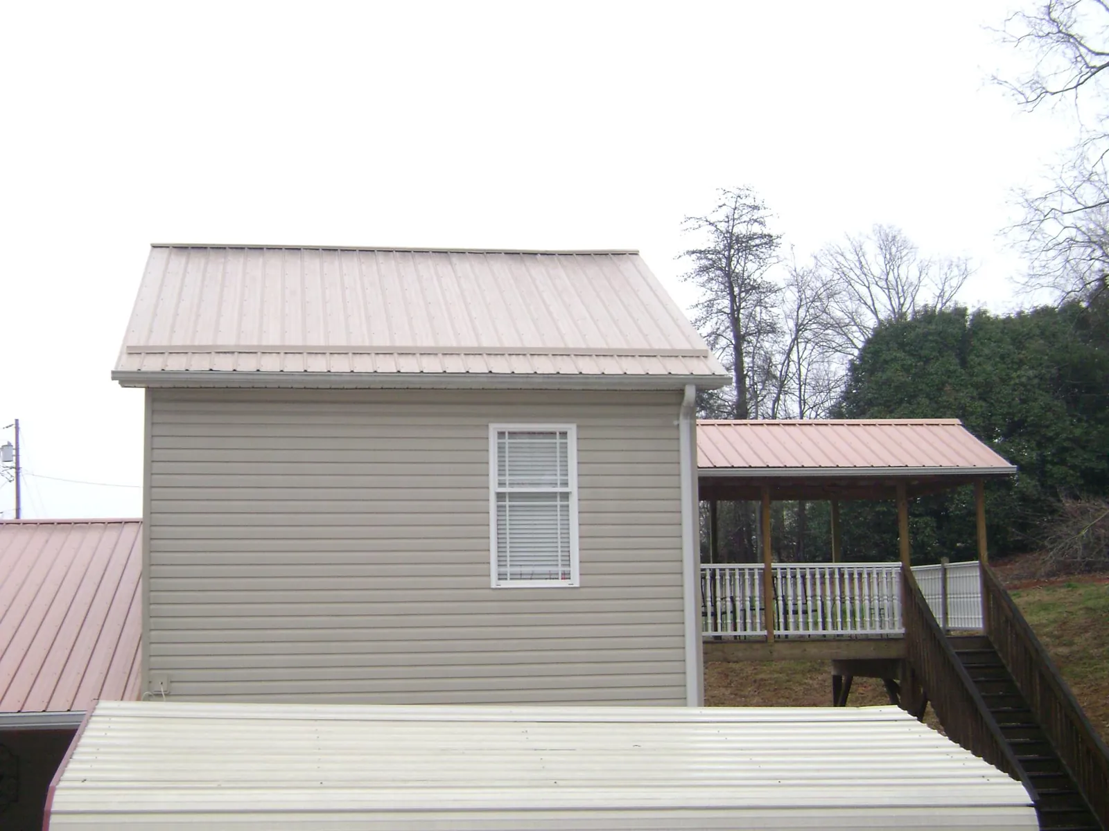Tan metal roofs on a two story addition and attached porch, from a Roof Replacement job in Rowena